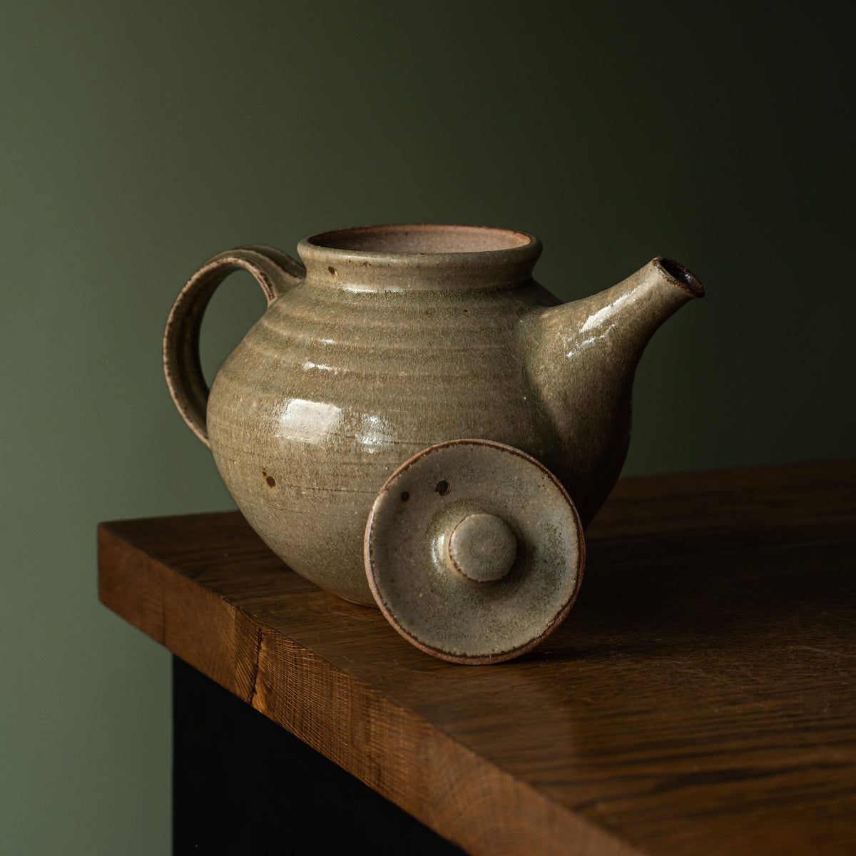 Leach Pottery handmade ceramic teapot in Ash green glaze with a rounded body, side pouring handle and spout with lid resting to the side of the pot.