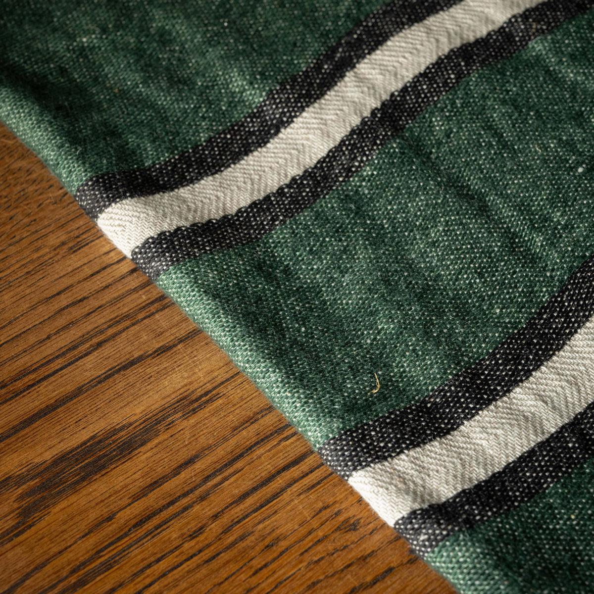 A close-up Libeco Belgian Towel with a washed racing green base and alternating black and bone stripes, laid over a brown wooden surface.
