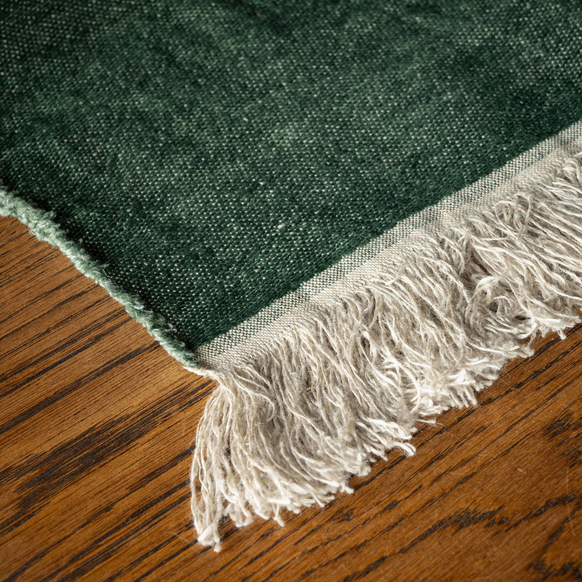 A close-up of Libeco Racing Green Belgian Linen Towel bone coloured fringes, laid on a brown wooden surface.