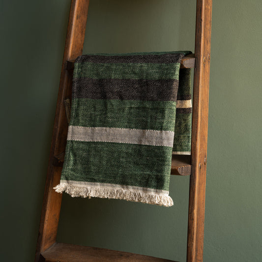 Libeco Belgian Linen Guest Towel. A washed linen hand towel in racing green with black and bone stripes, draped over a rustic wooden ladder against a dark green wall.