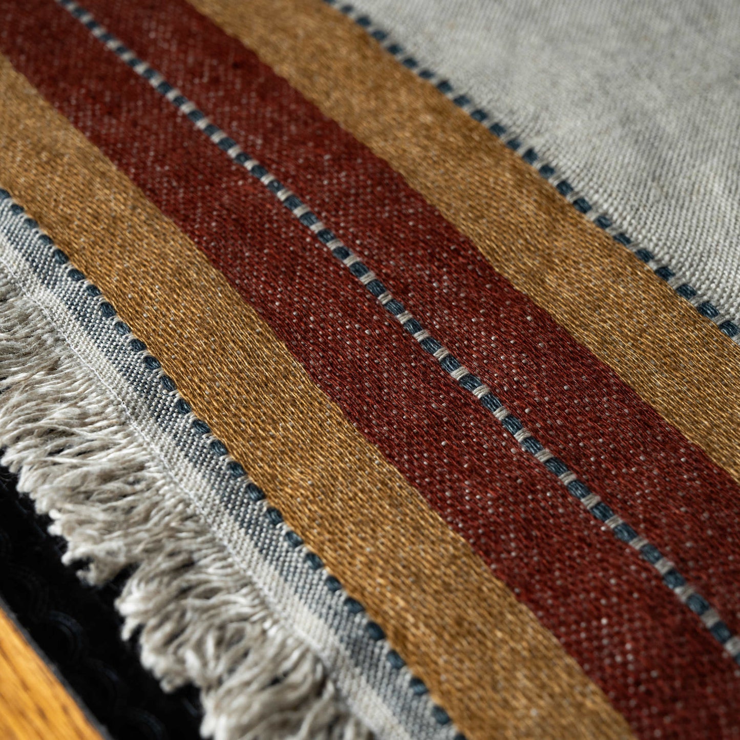 Close-up of a textured linen fabric of Libeco Hillside napkin with horizontal stripes in brown, red, and grey.
