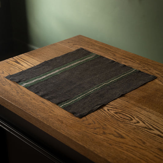Libeco Belgian Linen 'Stella' Napkin. A faded black base with racing green, bone and charcoal stripes, displayed on a rustic wooden table.