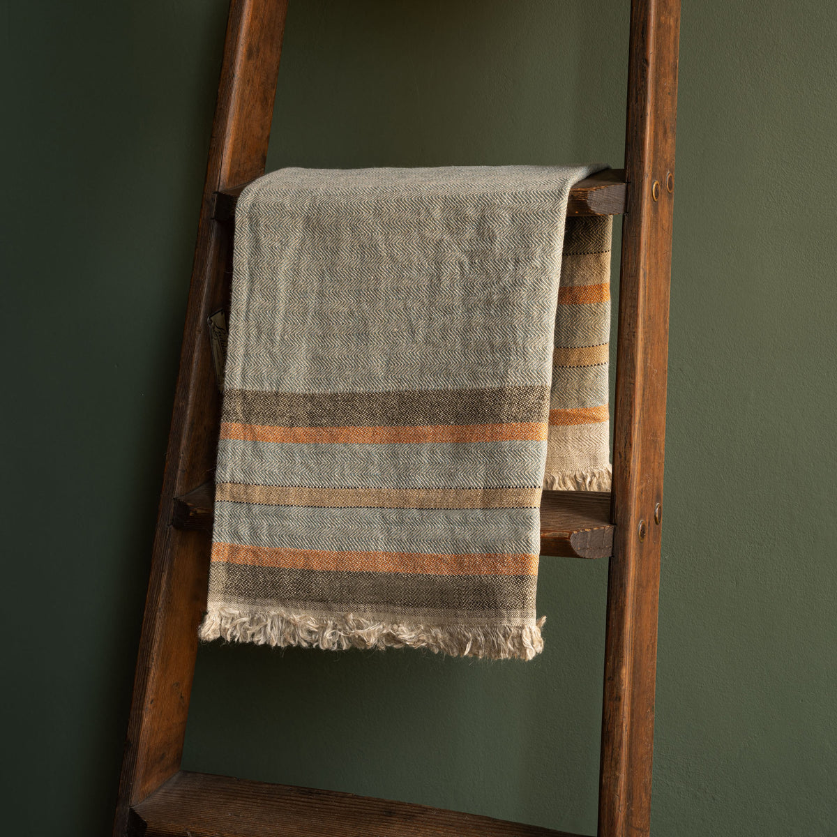 Libeco Belgian Linen multi stripe guest towel.  Woven hand towel with fringed edges draped over a rustic wooden ladder against a dark green wall.