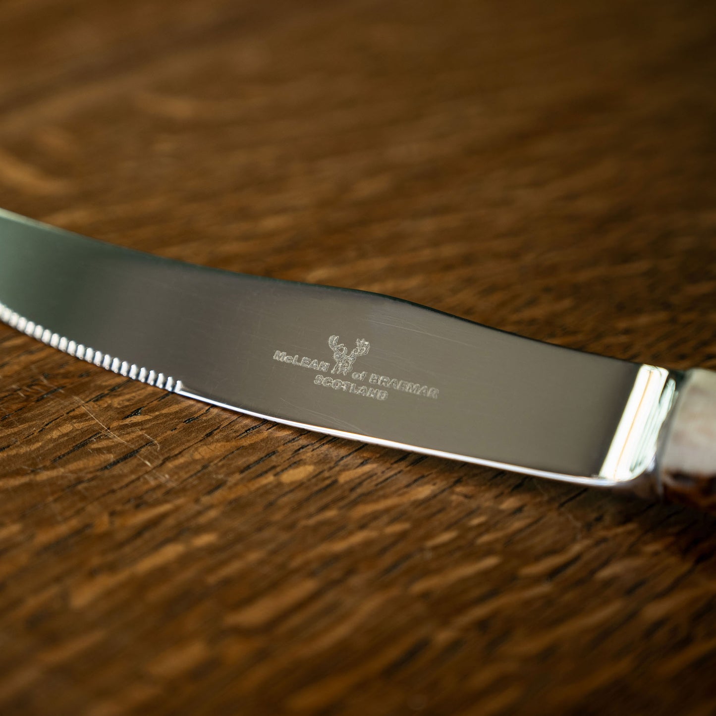 Close up of McLean of Braemar steel steak knife blade on a wooden surface
