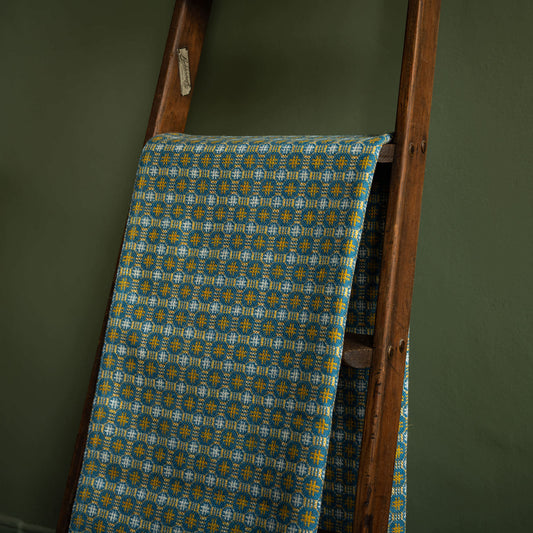 Melin Tregwynt Teils Welsh Blanket r draped over a wooden ladder against a green wall