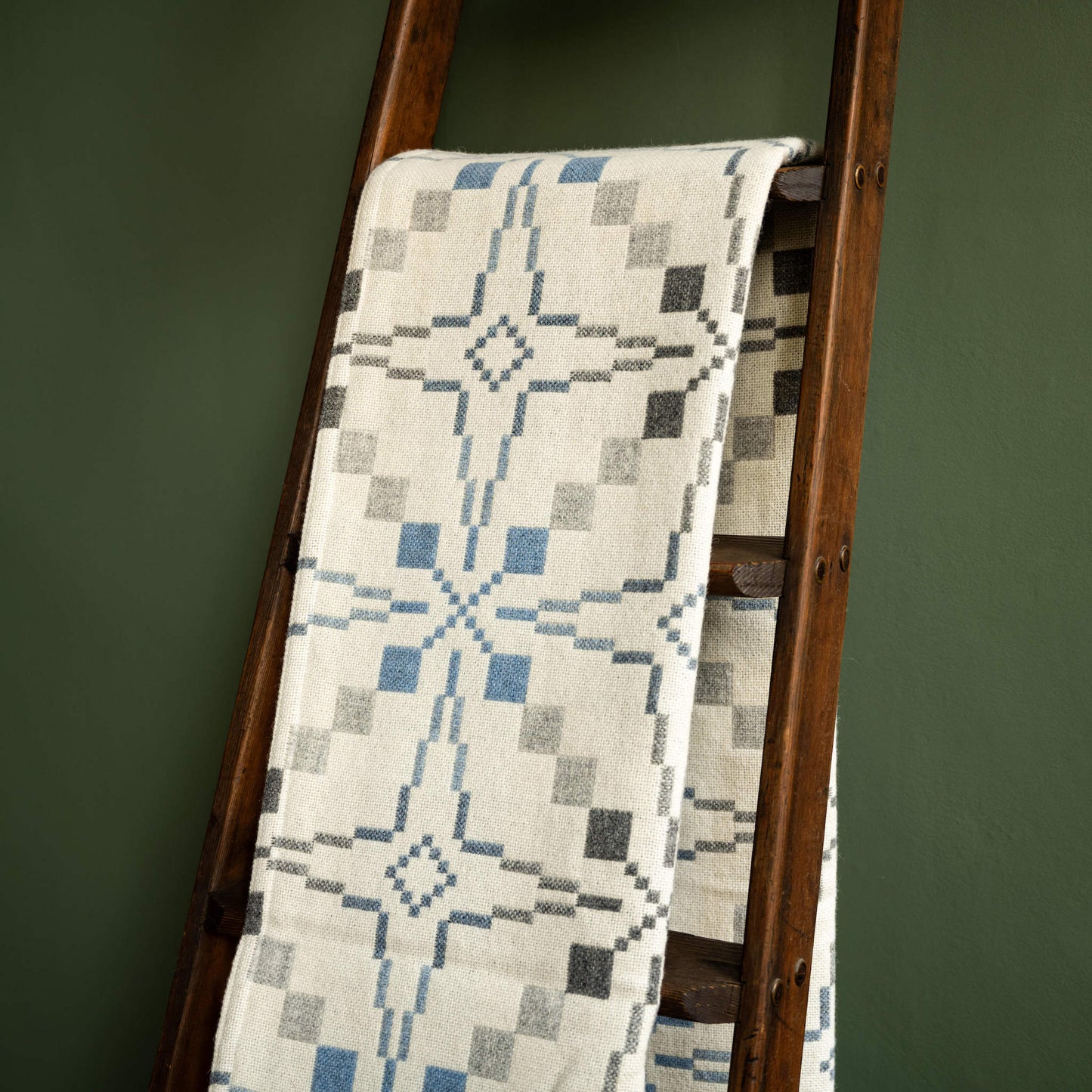 Melin Tregwynt Vintage Star Welsh Wool Blanket in Cynefin colourwayb draped over a wooden ladder