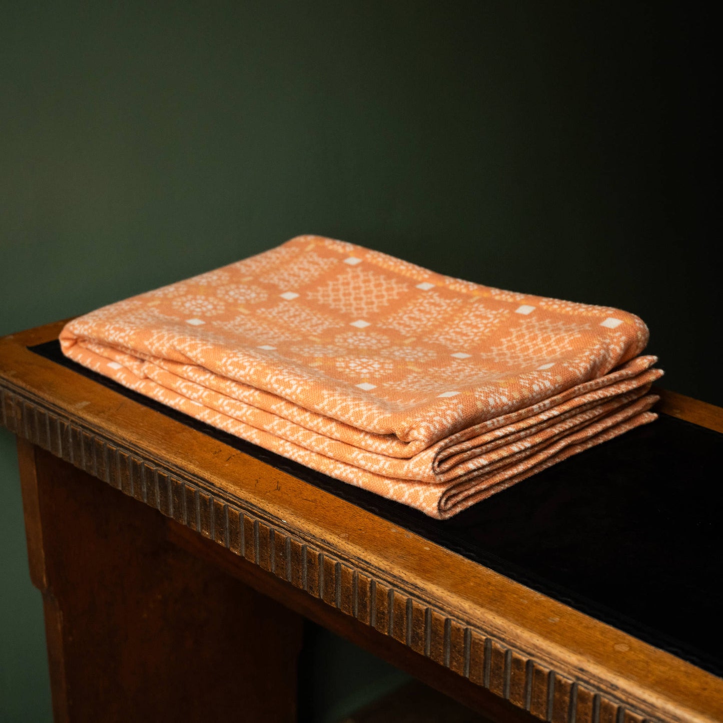 Melin Tregwynt Knot Garden Welsh Blanket in Cwrel colourway folded on a desk.