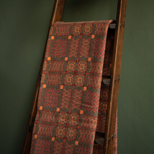 Melin Tregwynt copper Knot Garden Welsh wool blanket draped over a wooden ladder against a green wall