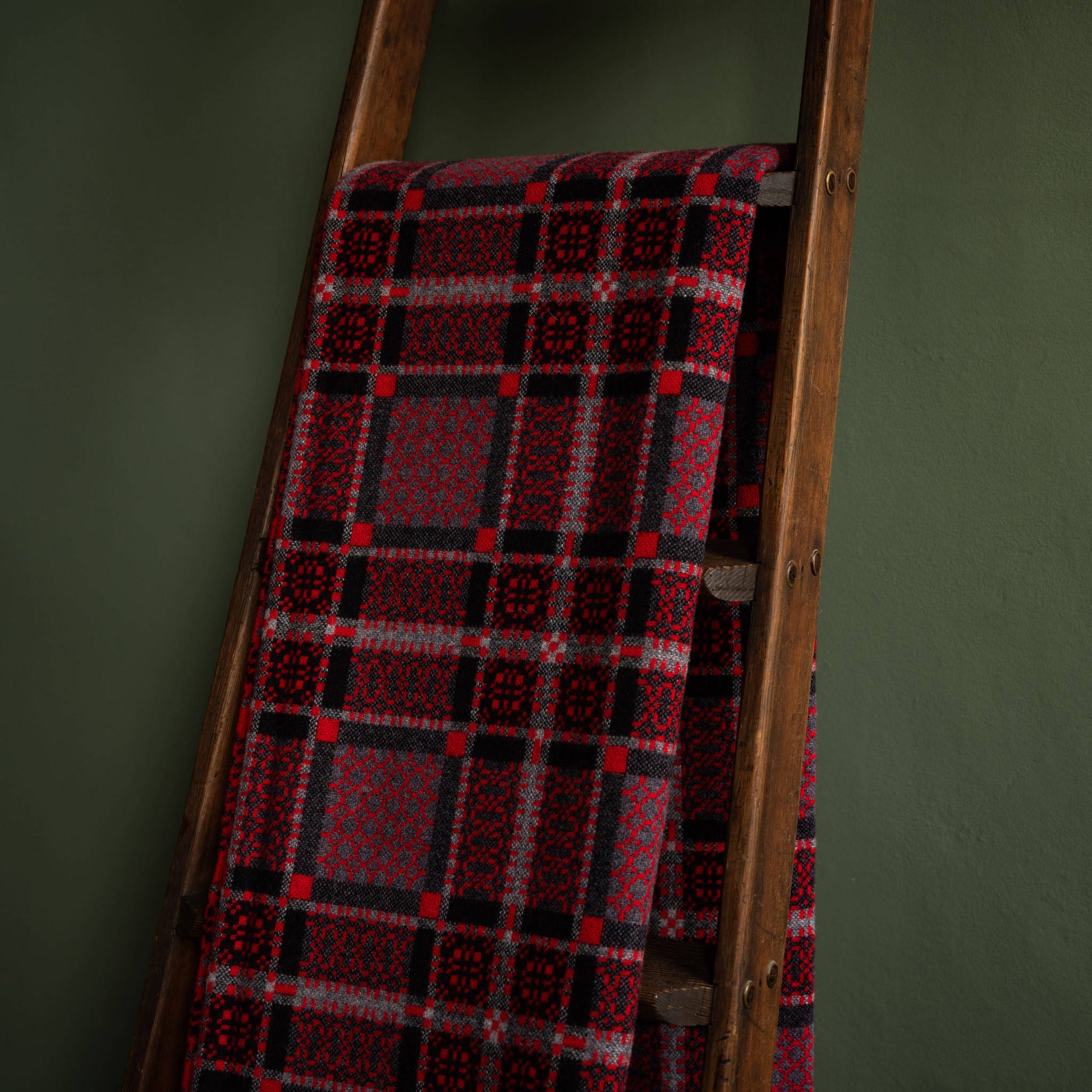 Reverse side of Melin Tregwynt Draig Welsh Blanket draped over a wooden ladder against a green wall