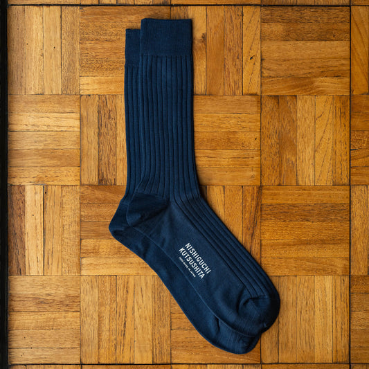 Nishiguchi Kutsushita navy silk and cotton ribbed socks, laid flat on a wooden parquet surface.
