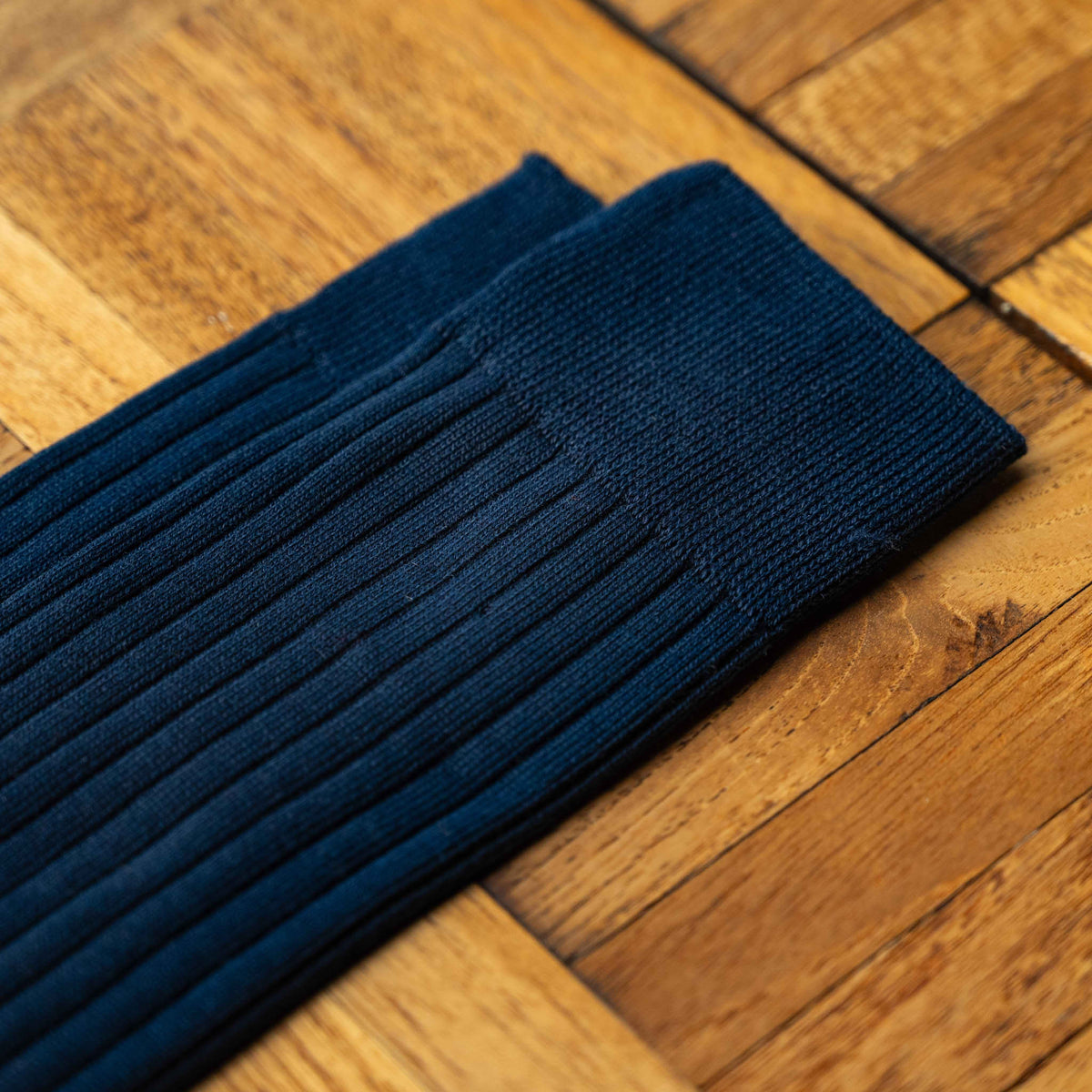 A close-up of Nishiguchi Kutsushita  dark navy blue silk and cotton ribbed socks laid diagonally showing the top cuff detail.