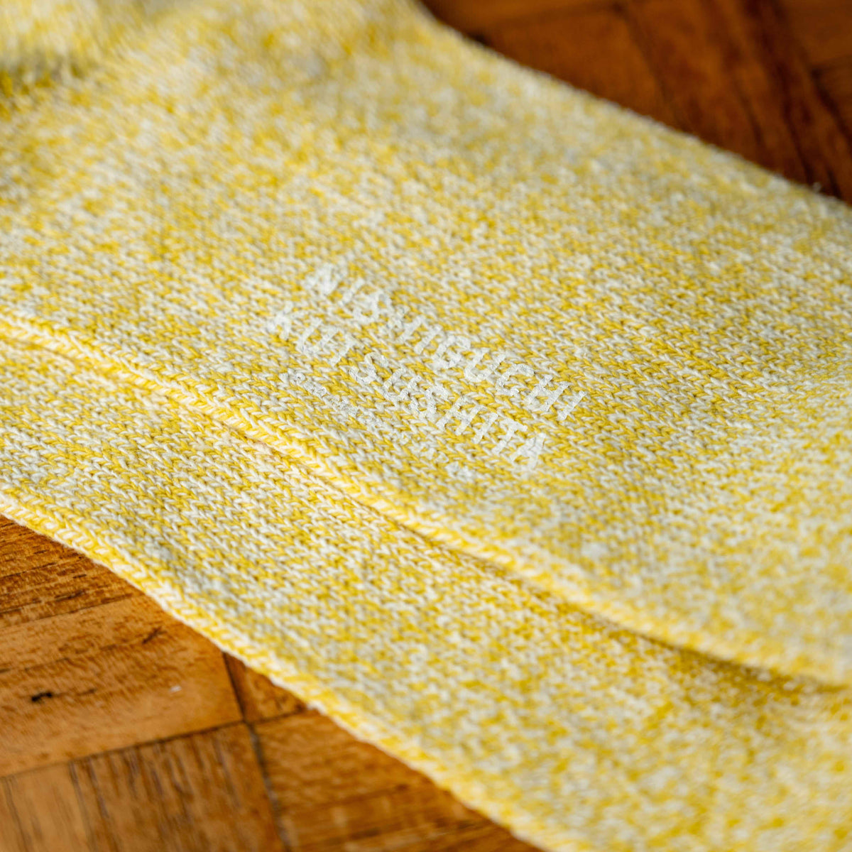 A close-up of Nishiguchi Kutsushita yellow silk and cotton knit sock sole with white text showing the makers brand name.