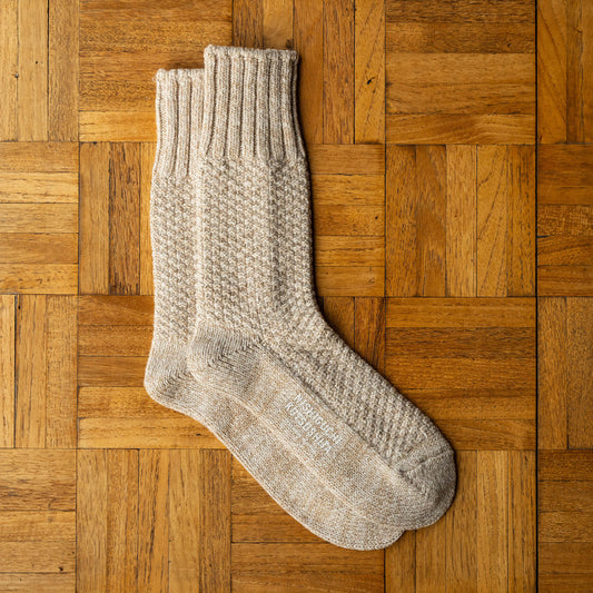 Nishiguchi Kutsushita beige cable-knit wool and cotton boot socks, laid flat on a wooden parquet surface.