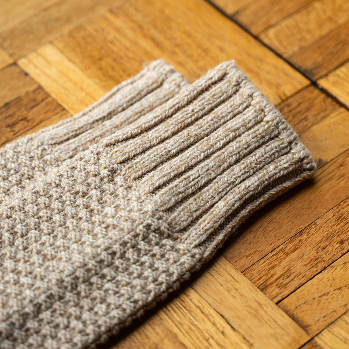 A close-up of Nishiguchi Kutsushita ribbed wool and cotton boot socks in a beige colour, laid diagonally showing the top cuff detail.