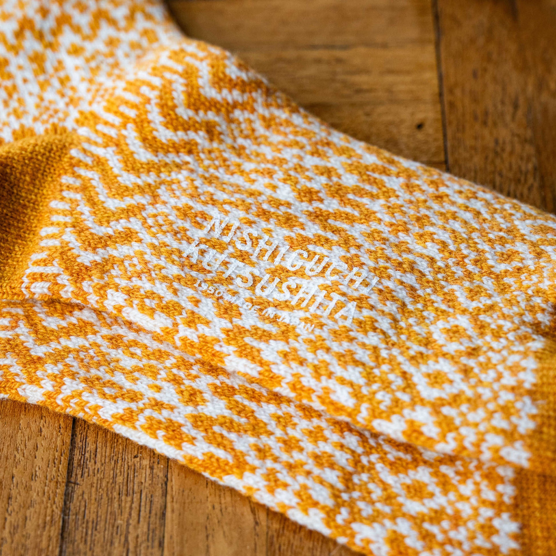 Wool jacquard socks in lantern orange with white geometric design  & 'Nishiguchi Kutsushita' branding on the sole