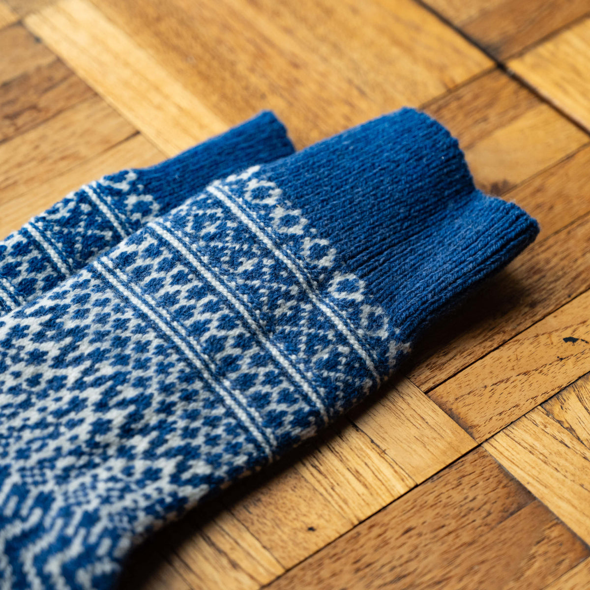 A pair of Nishiguchi Kutsushita blue and white wool jaquard patterned knit socks laid diagonally showing the top cuff detail.