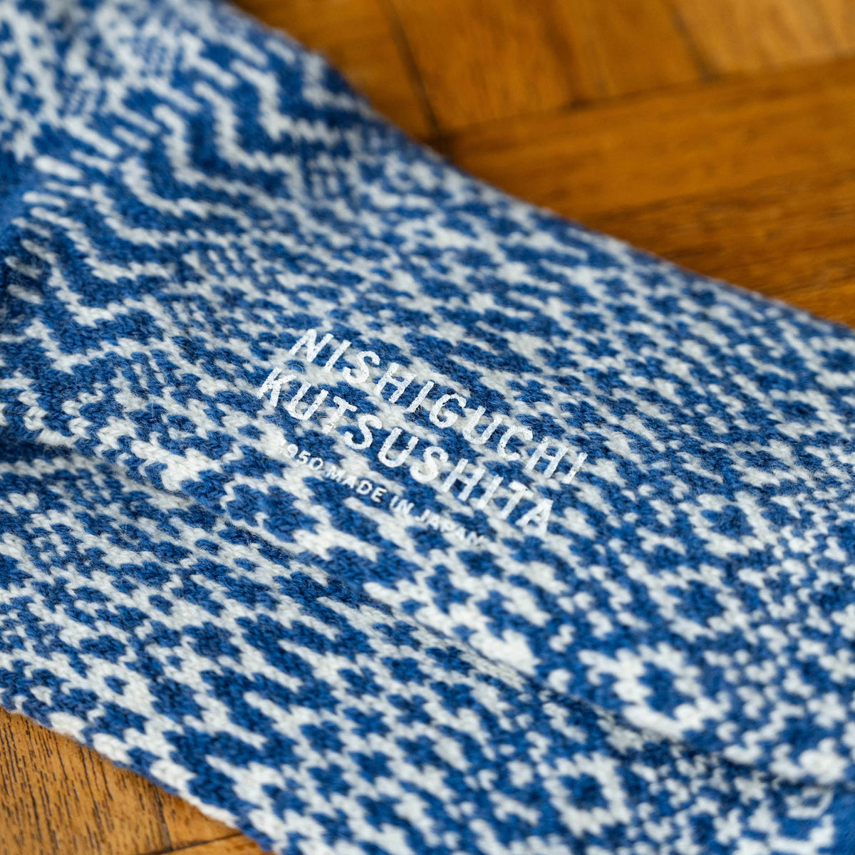 A close-up of Nishiguchi Kutsushita blue and white wool jacquard patterned knit socks sole with brand logo.