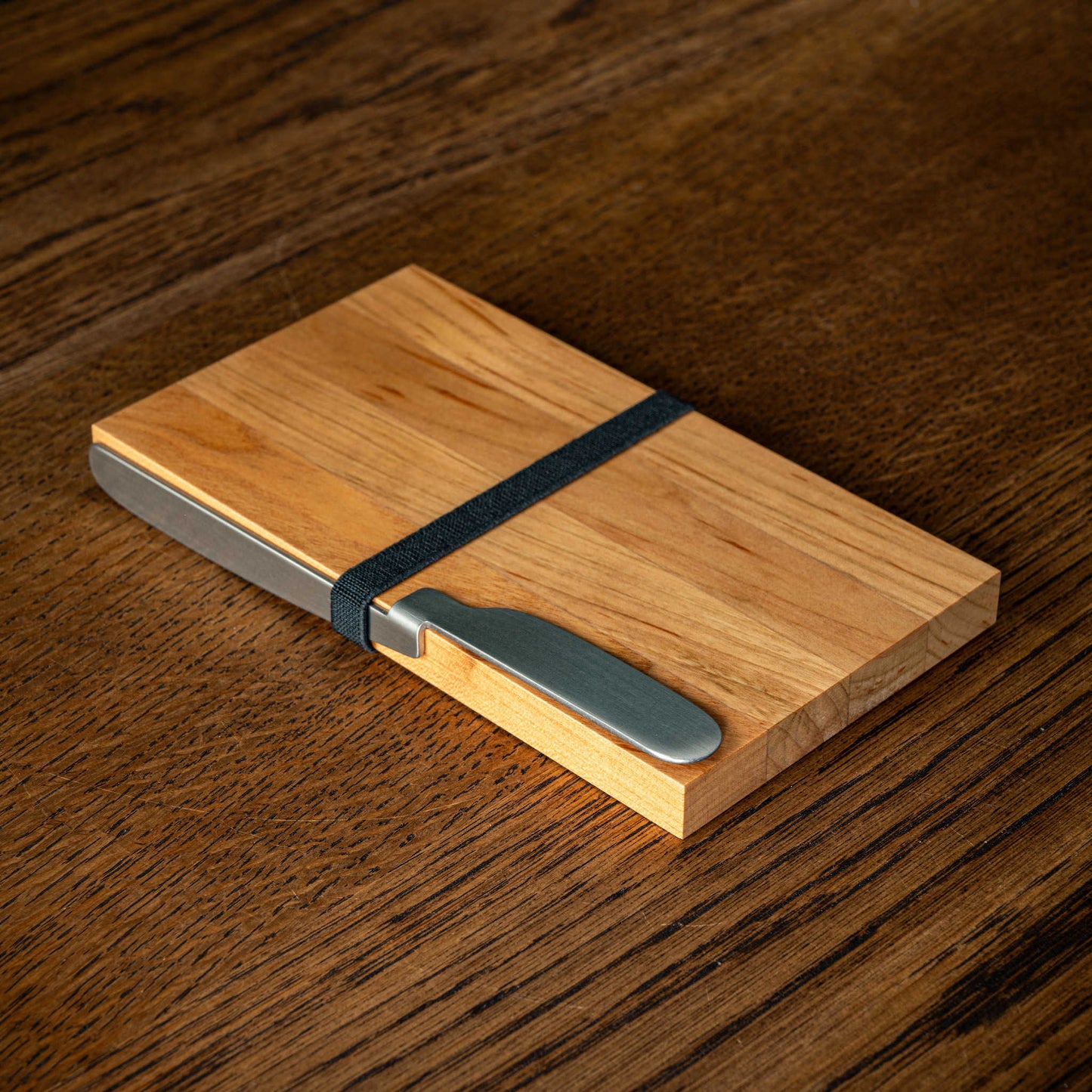 OKU Board. Designed by Kathleen Reilly. A folded stainless steel spreader knife resting on a the rectangular OKU wooden cutting board.
