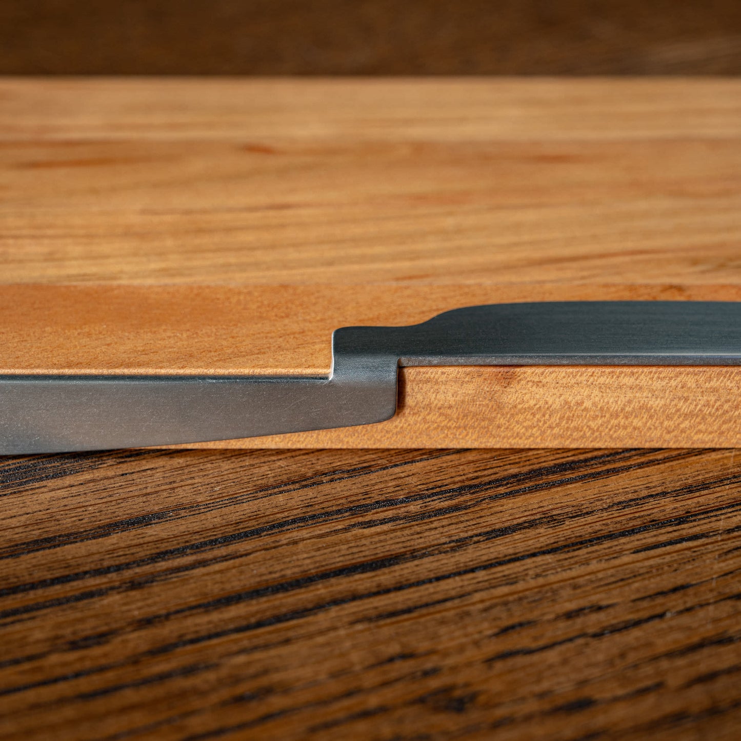 A close-up of the OKU folding stainless steel knife resting in place on the OKU board. 