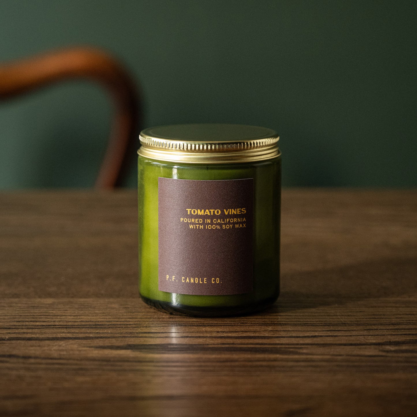 PF Candle Co Tomato Vines scented candle in a green glass jar with a gold lid on a wooden surface against a dark green background