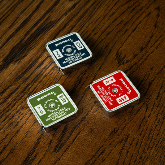 Penco pocket tape measures, navy, green and red versions on a wooden surface.
