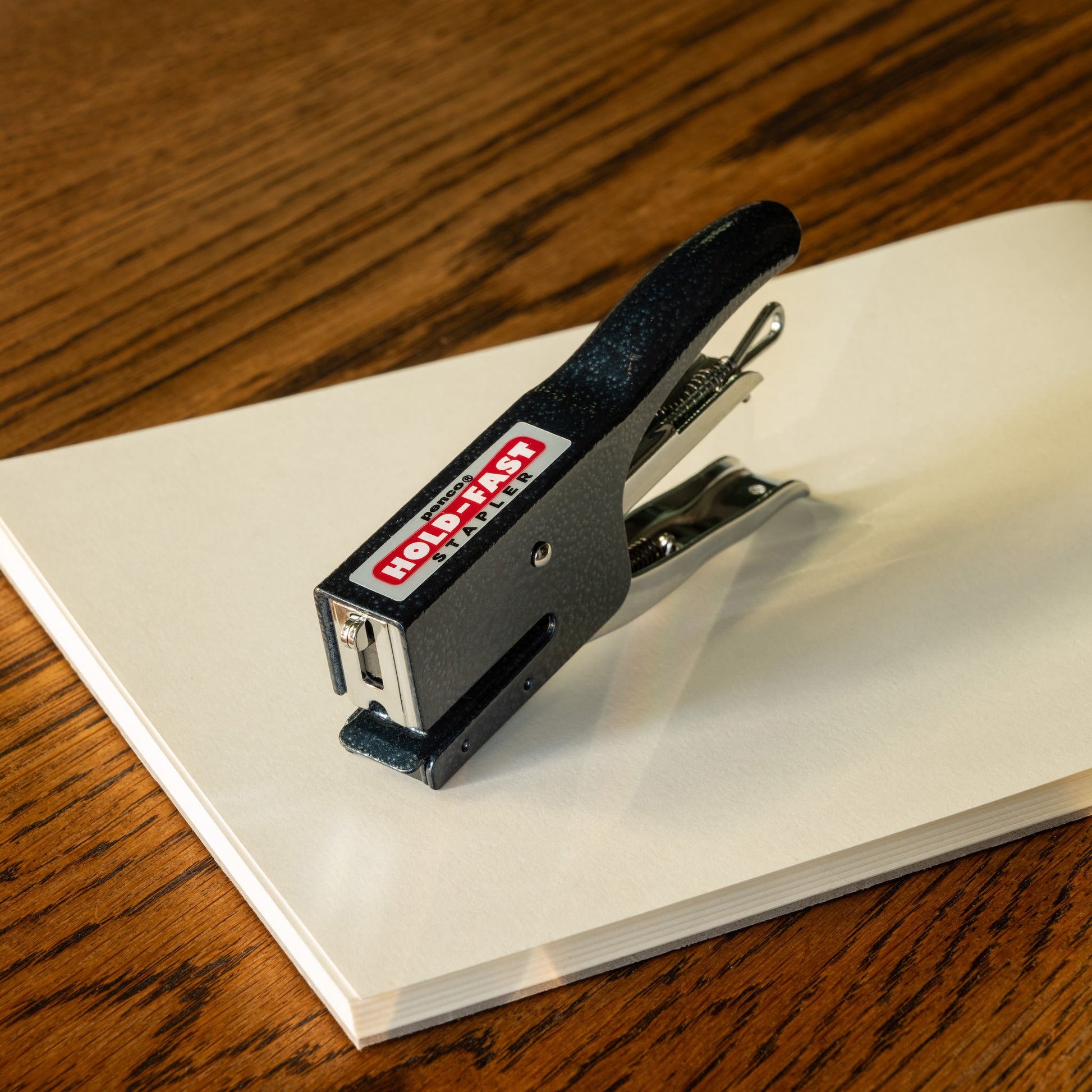 Navy Penco stapler on a white sheet of paper with a wooden surface underneath