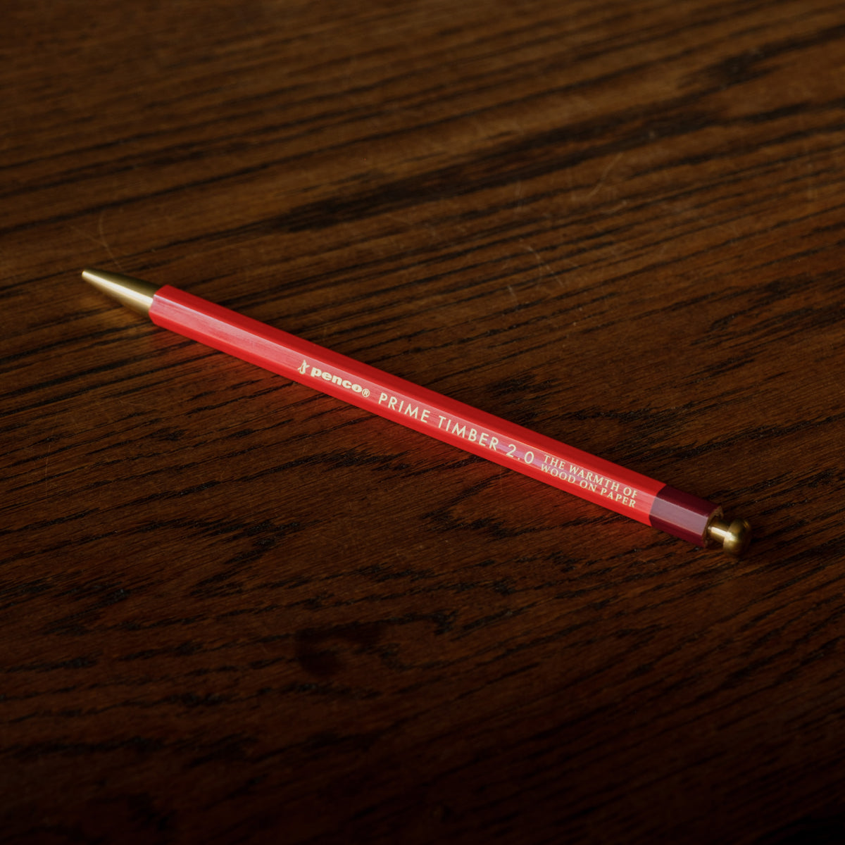 Penco Prime Timber 2-0 mechanical  pencil with brass fittings, resting on a dark brown wooden surface.
