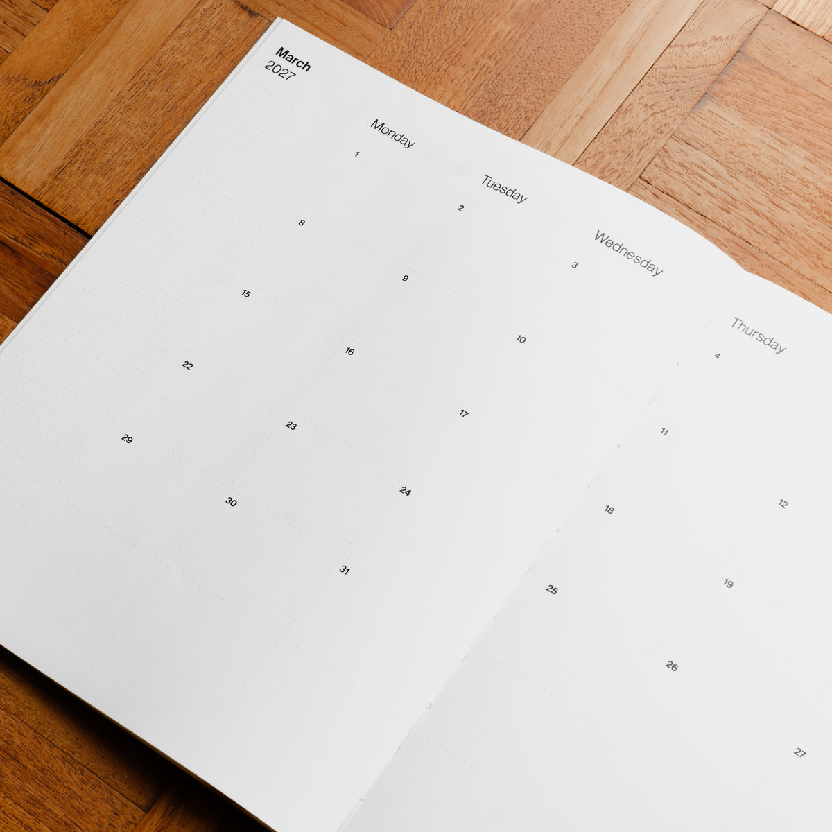 Pith Supply minimalist monthly calendar page for March 2027 printed on white paper, laid flat on a warm brown wooden surface.