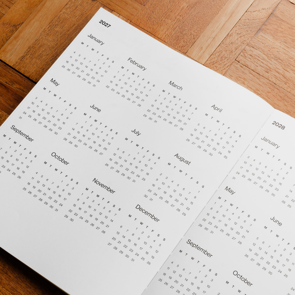 Pith Supply Pomelo Planner year-at-a- glance calendar page showing the months of 2027 and 2028 in a clean grid layout on white paper, photographed on a warm wooden surface.