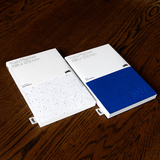 Two Pith Supply Yuzu 2027 Planners. One with a white speckled seaweed paper cover and one with a bright blue cover both embossed with 2027 date. 