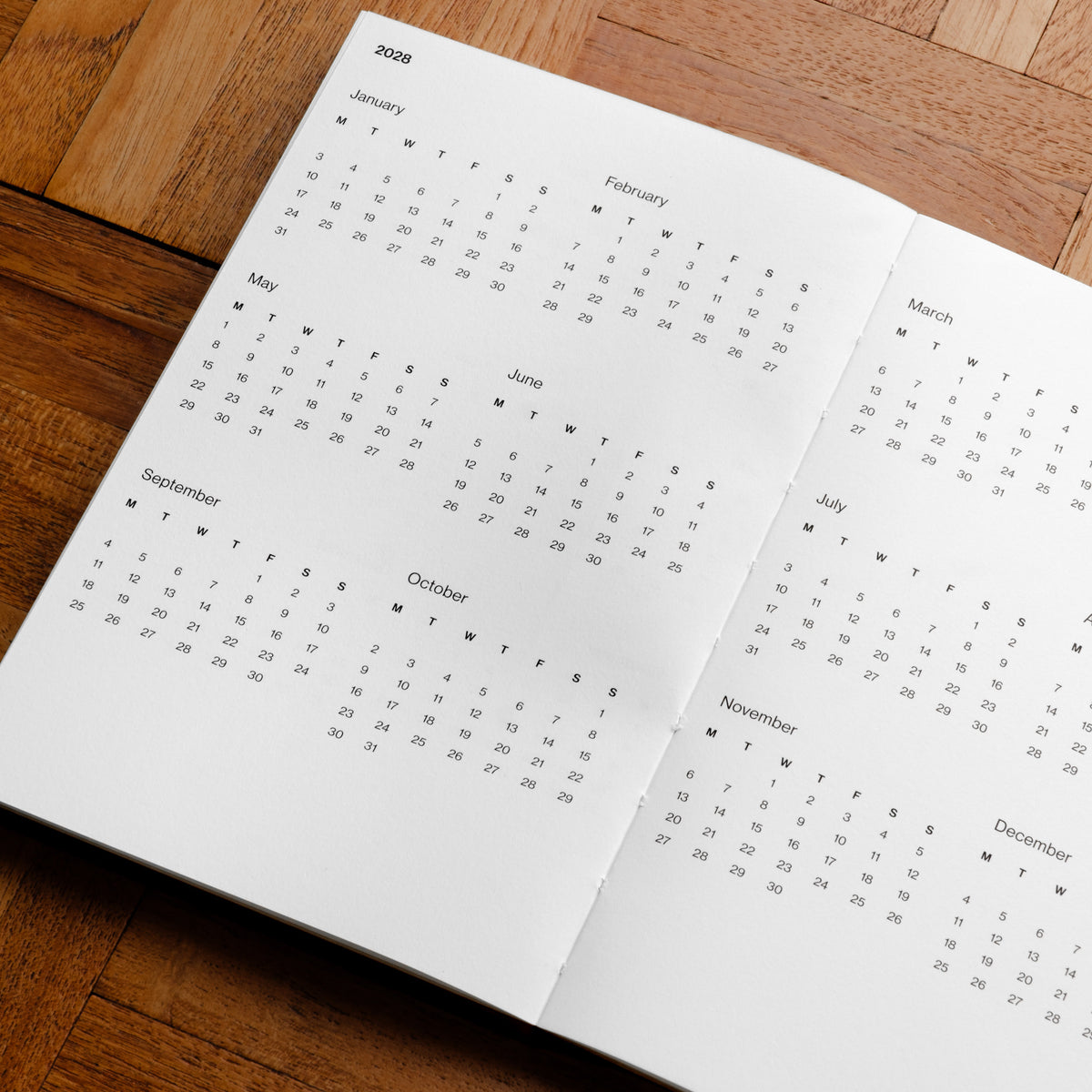 Pith Supply YUuzu Planner 2028 calendar spread on a wooden surface, showing monthly calendar grids in black text.