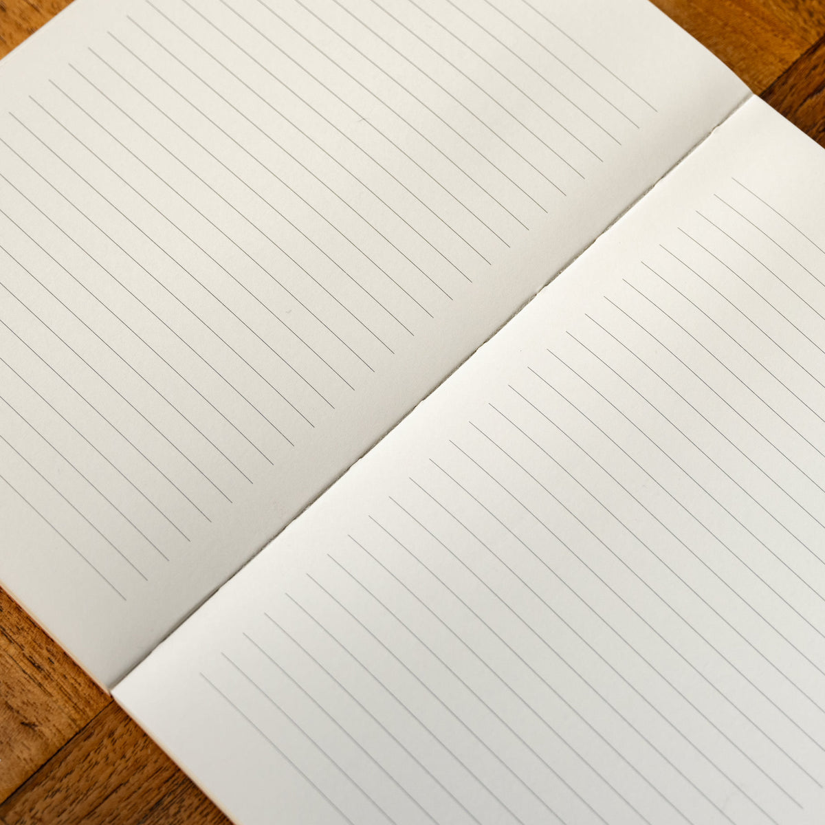 A close-up of Yuzu notebook page in off-white paper with a ruled lined layout in black, placed on a wooden surface.