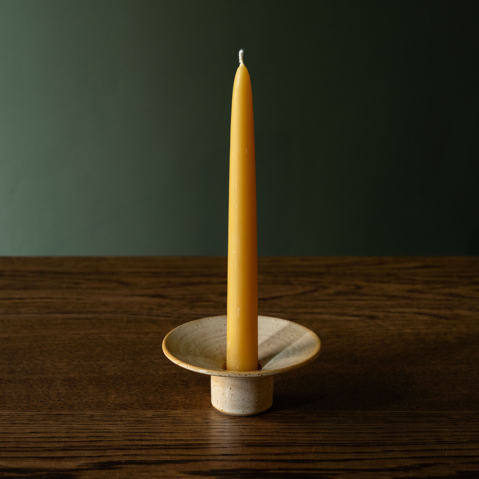 Pottery West standard dinner candle holder in sand flecked stoneware with a beeswax dinner candle on a wooden table