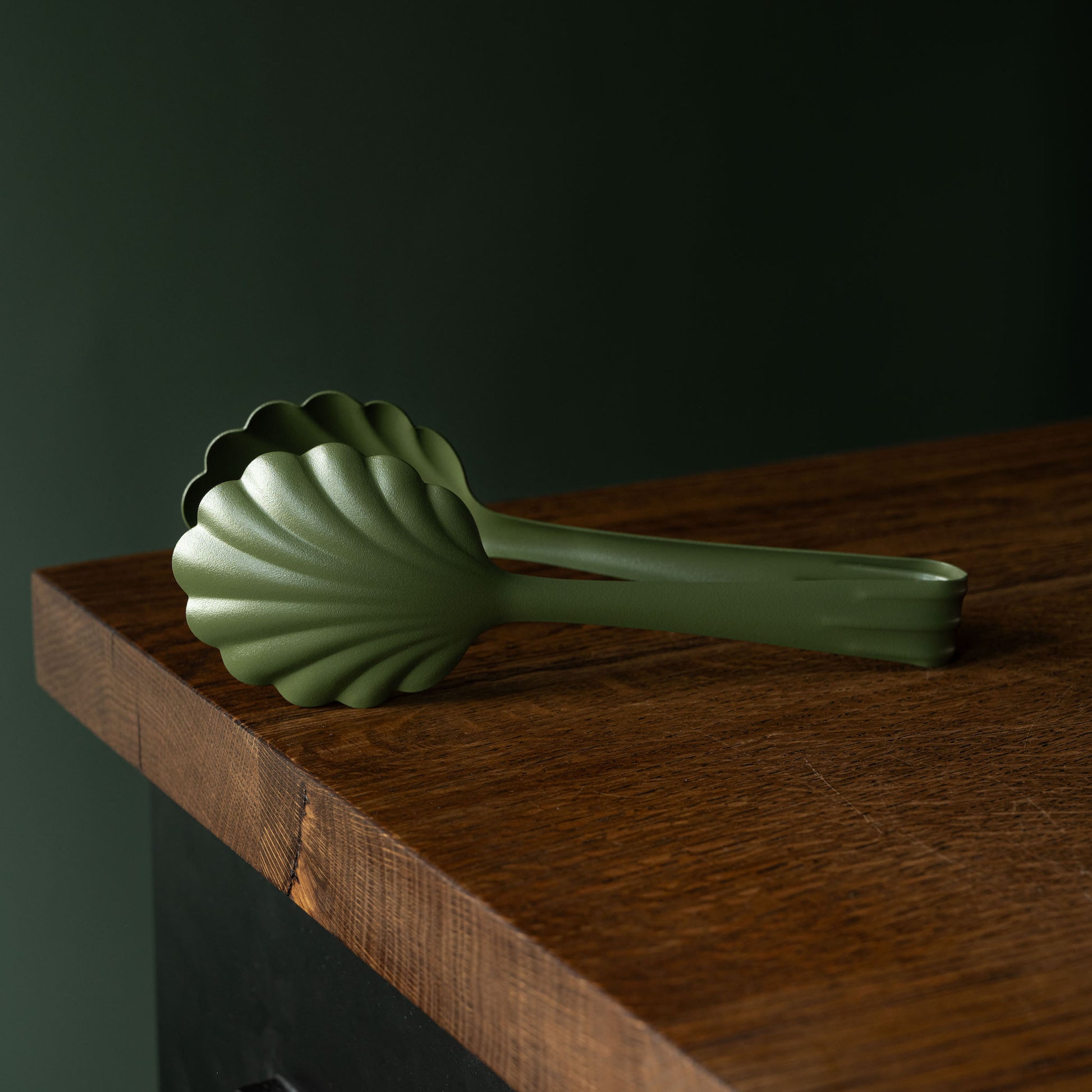 Khaki green Roger Orfevre steel bakery tongs on a wooden surface 