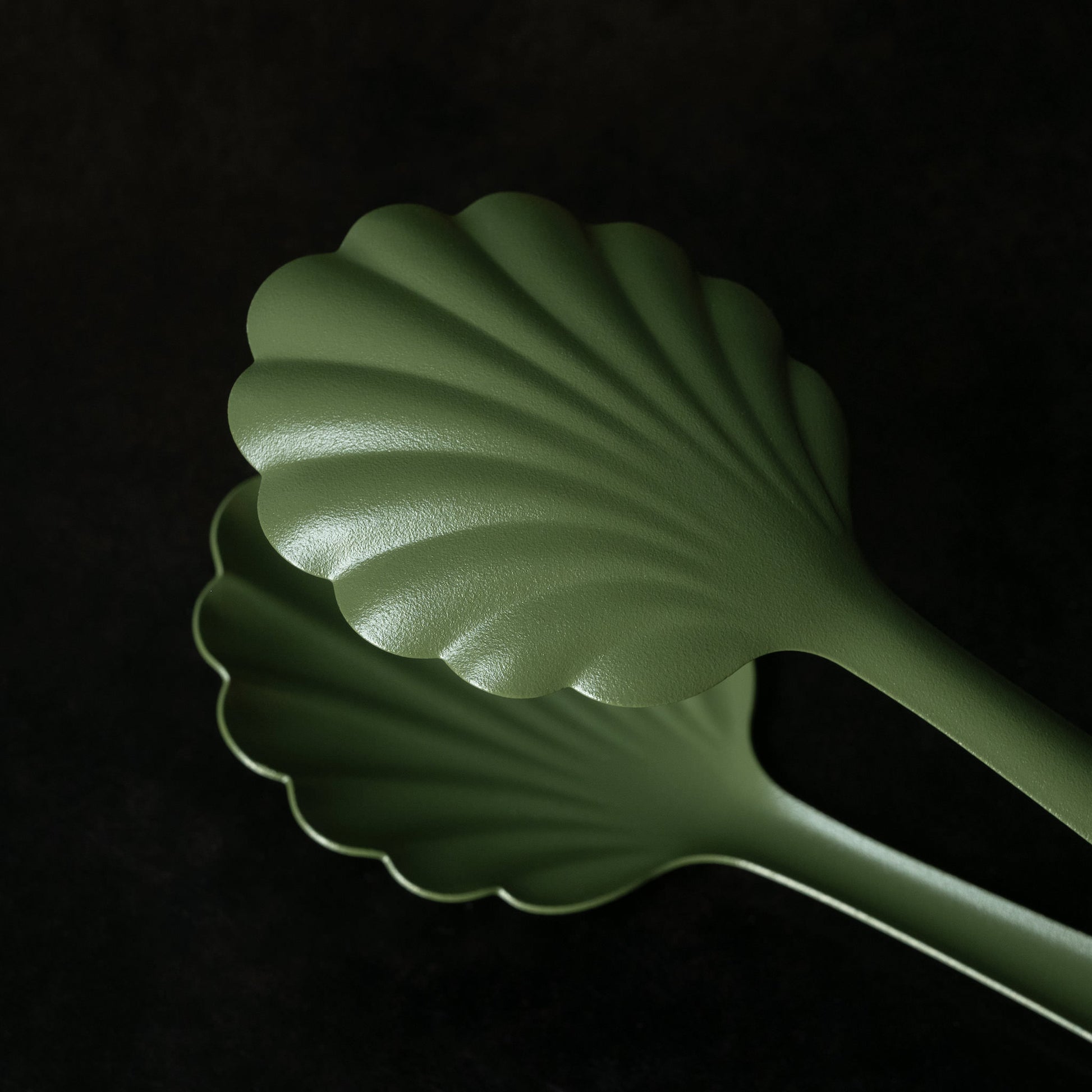 Close up of khaki green scalloped-shaped Roger Orfevre steel bakery tongs  