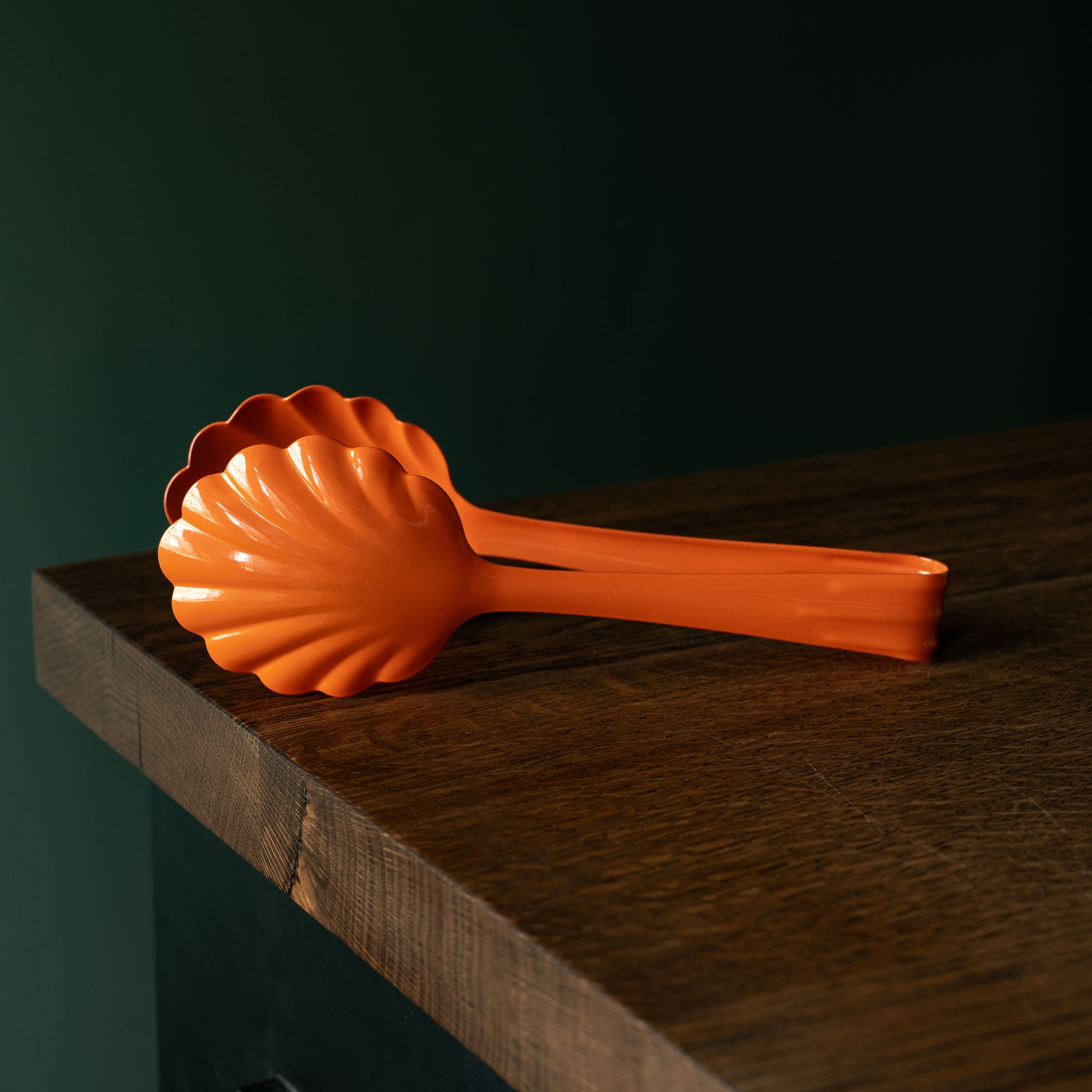 Orange Roger Orfevre scallop-shaped steel bakery tongs on a wooden surface