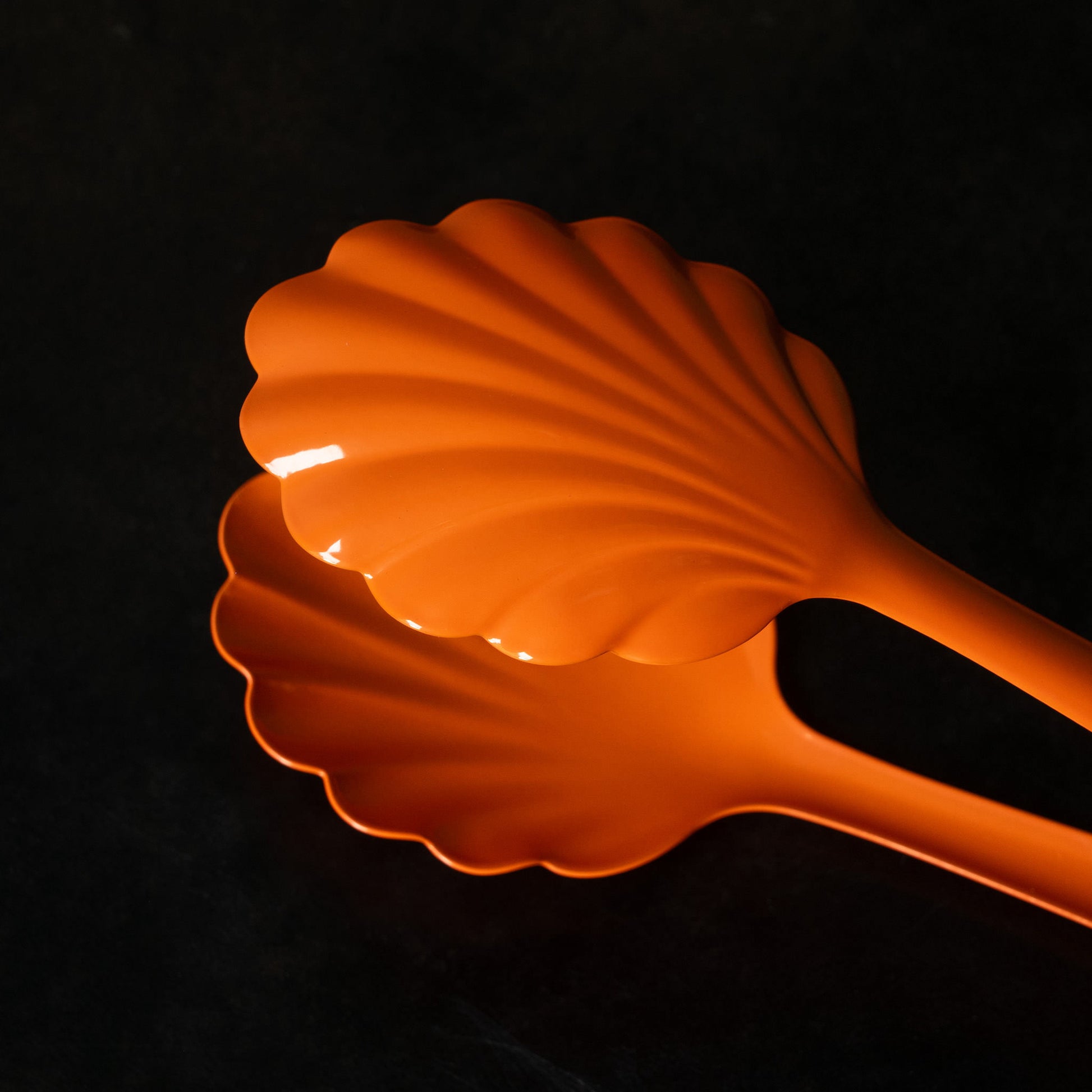Close up of orange Roger Orfevre scallop-shaped steel bakery tongs 