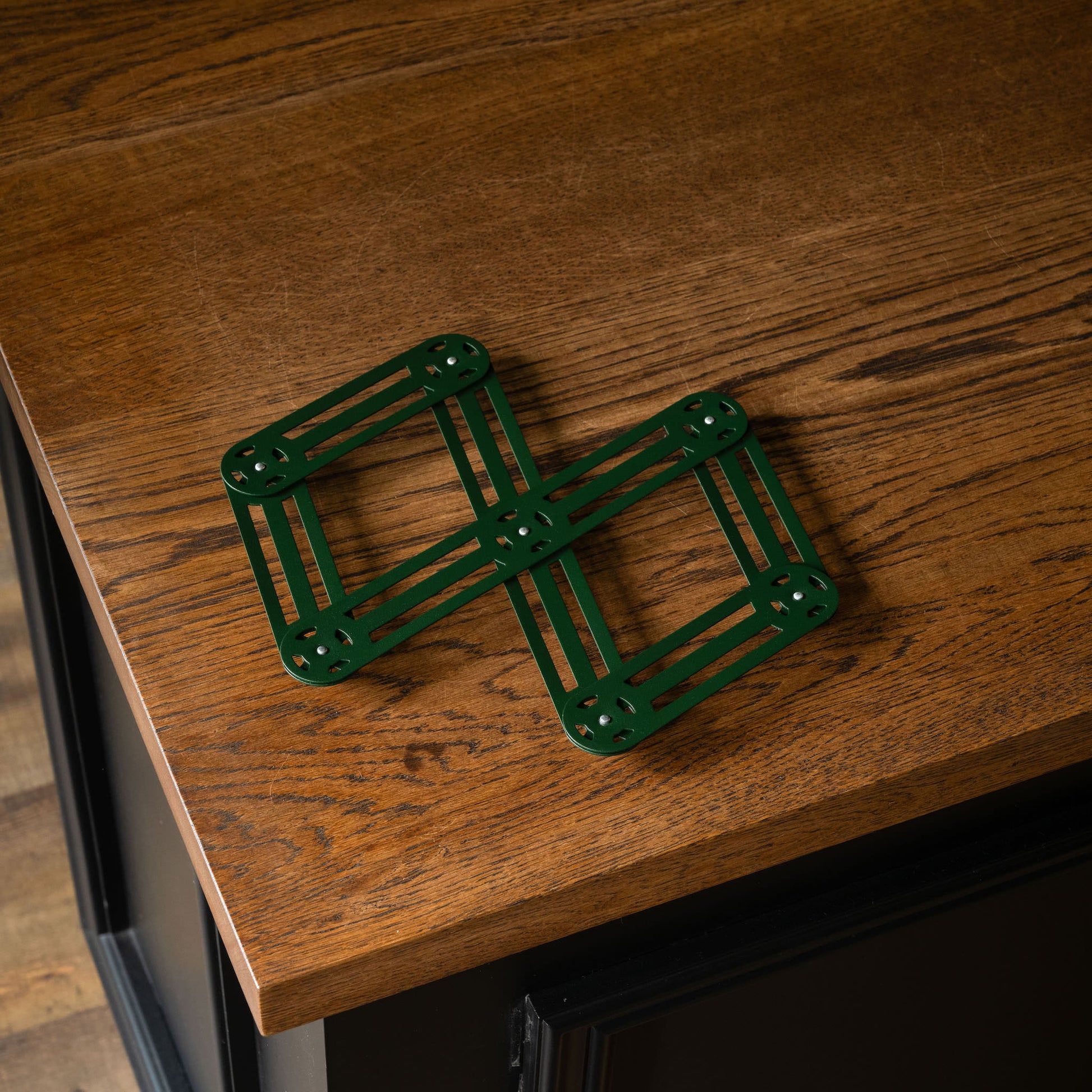 Roger Orfevre pine green steel  adjustable trivet on a wooden surface