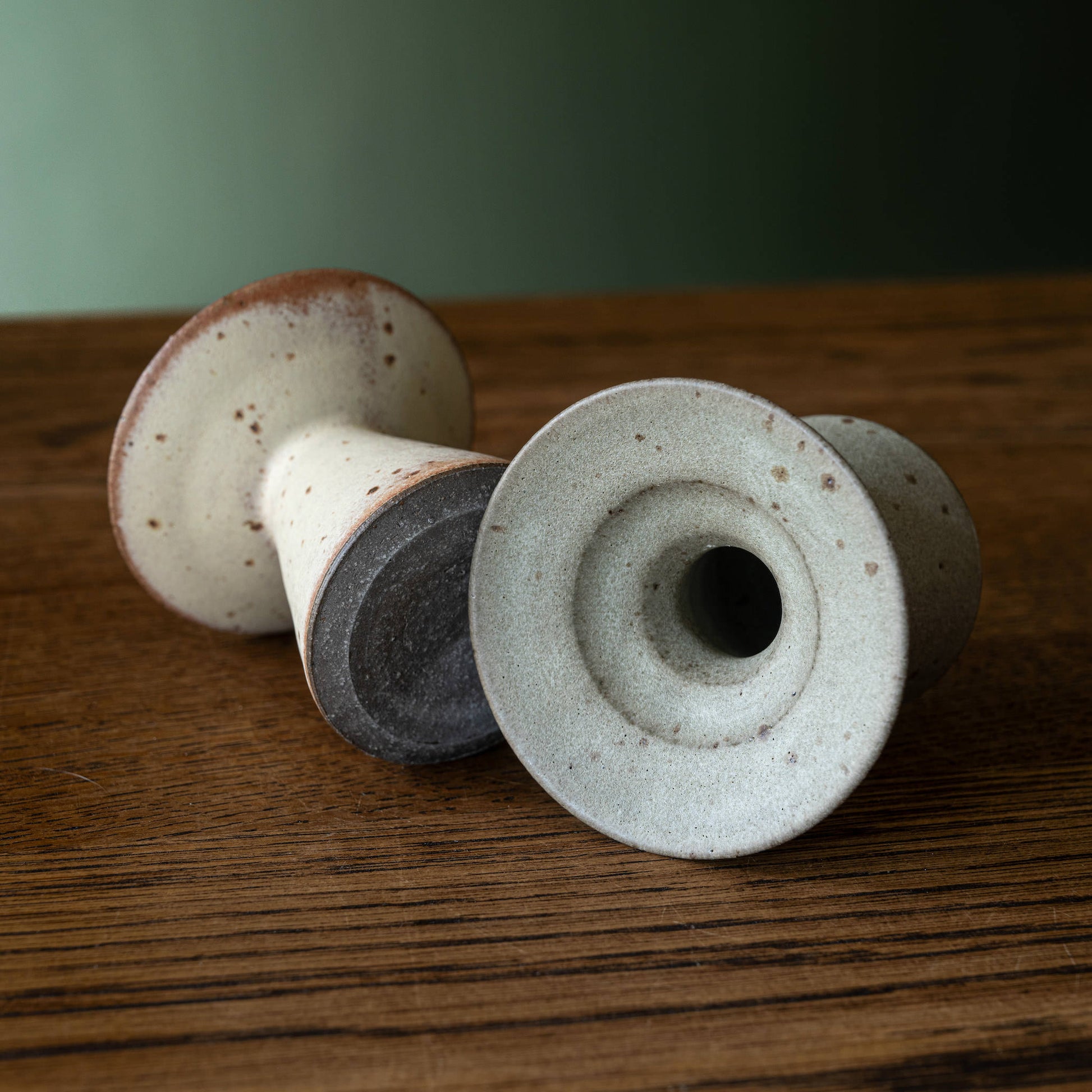 Two ceramic candleholders by Studio Brae with speckled cream and grey glazes, displaying the top and base.