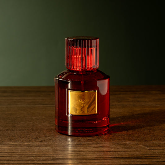A bottle of Trudon 45 Eau de Parfum, housed in a red translucent glass bottle red with a gold label and a ribbed red cap, sitting on a dark wooden table against a dark green background.