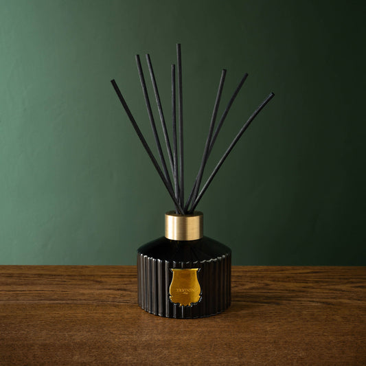 Trudon Gabriel Reed Diffuser in dark green glass bottler with gold accents on a wooden surface against a green wall