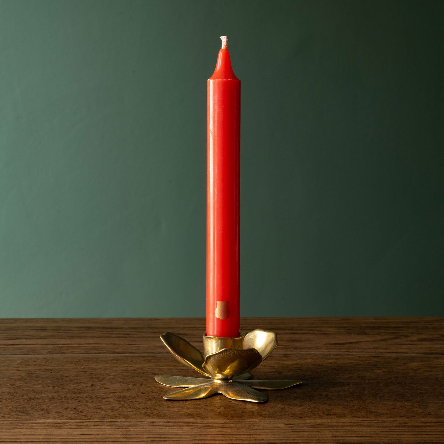 Trudon brick Madeleine taper candle in a gold candle holder on a wooden surface with a green background