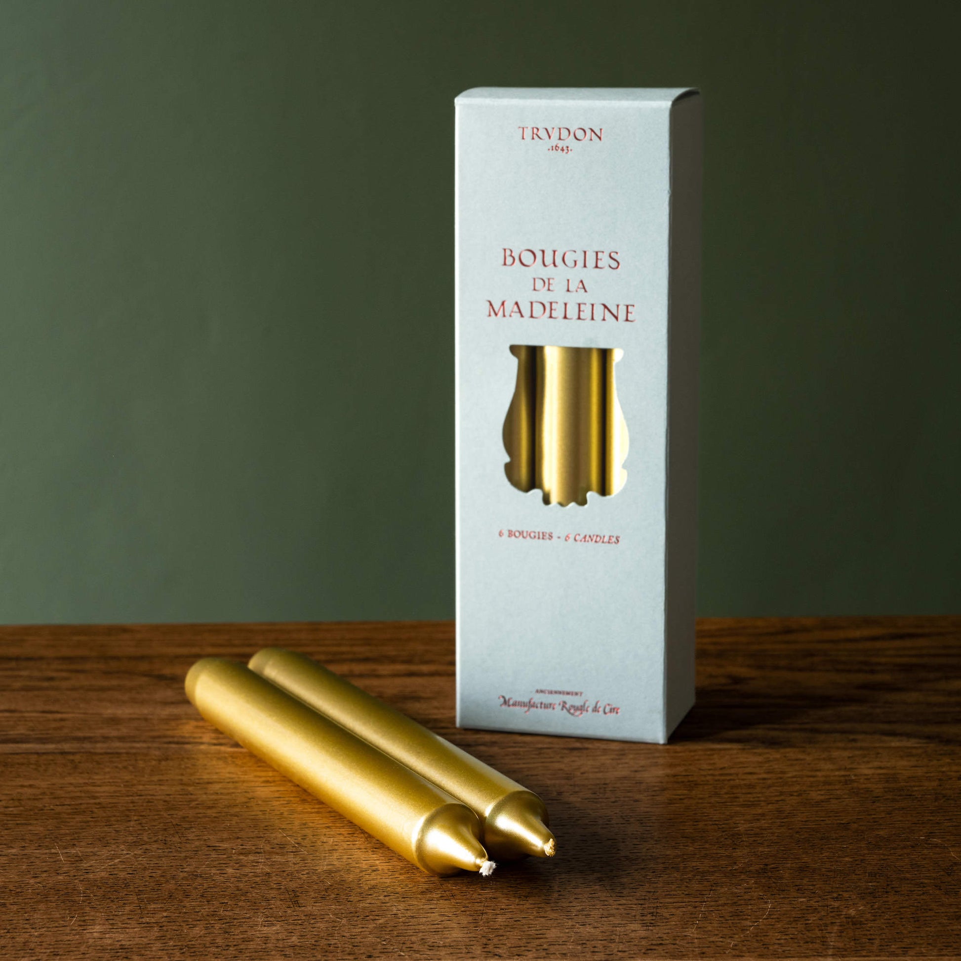 Trudon Madeleine Taper Candles box of 6 with two gold candles on a wooden surface.