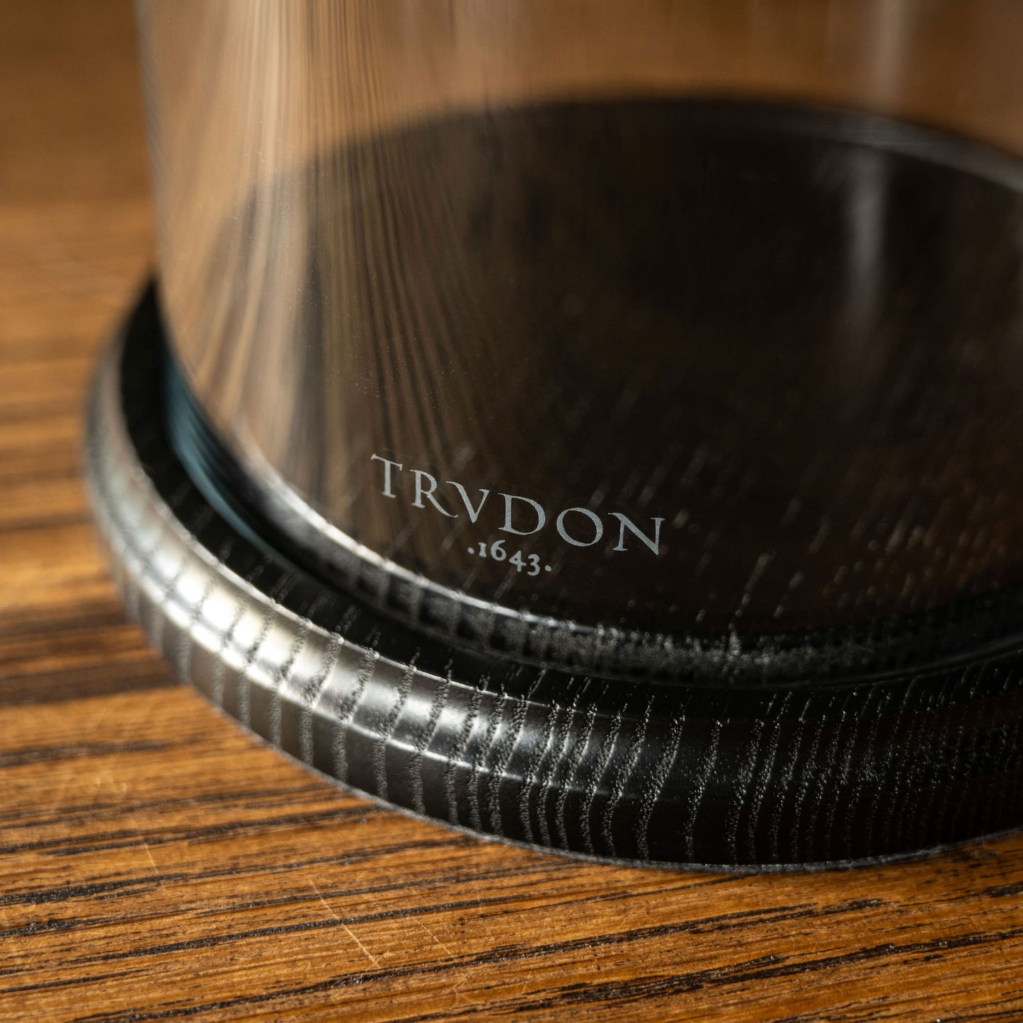 Close-up of the dark textured wooden base of the Trudon La Cloche with the brand name TRUDON 1643 etched on to the glass bell jar.