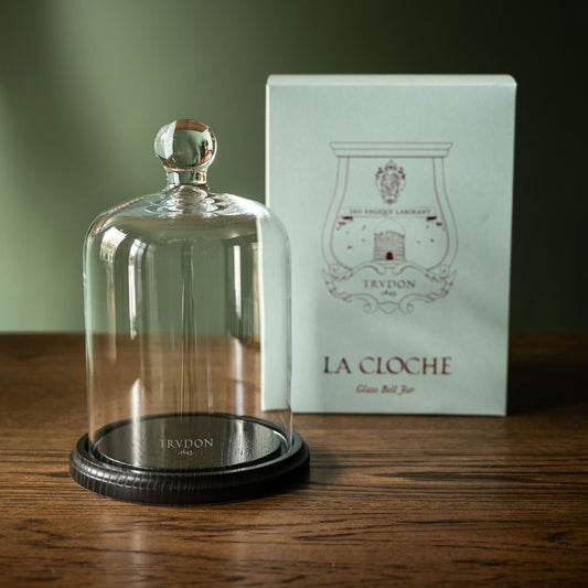 Trudon La Cloche. A glass bell jar with a dark wood base, shown next to it's box on a wooden table.