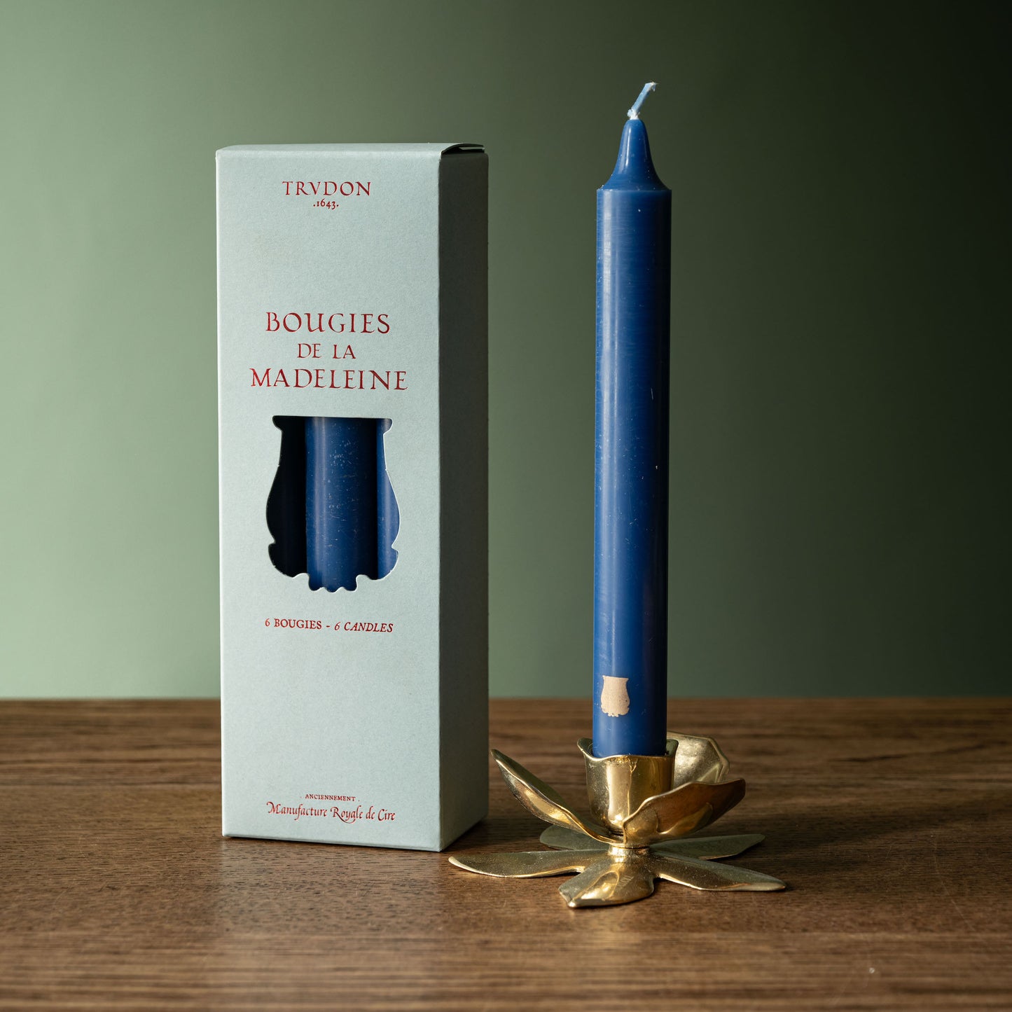 Trudon Madeleine Taper Candle in Bleu Marine in Trudon Flower Candle stick next to a box of 6 Madeleine Candles.