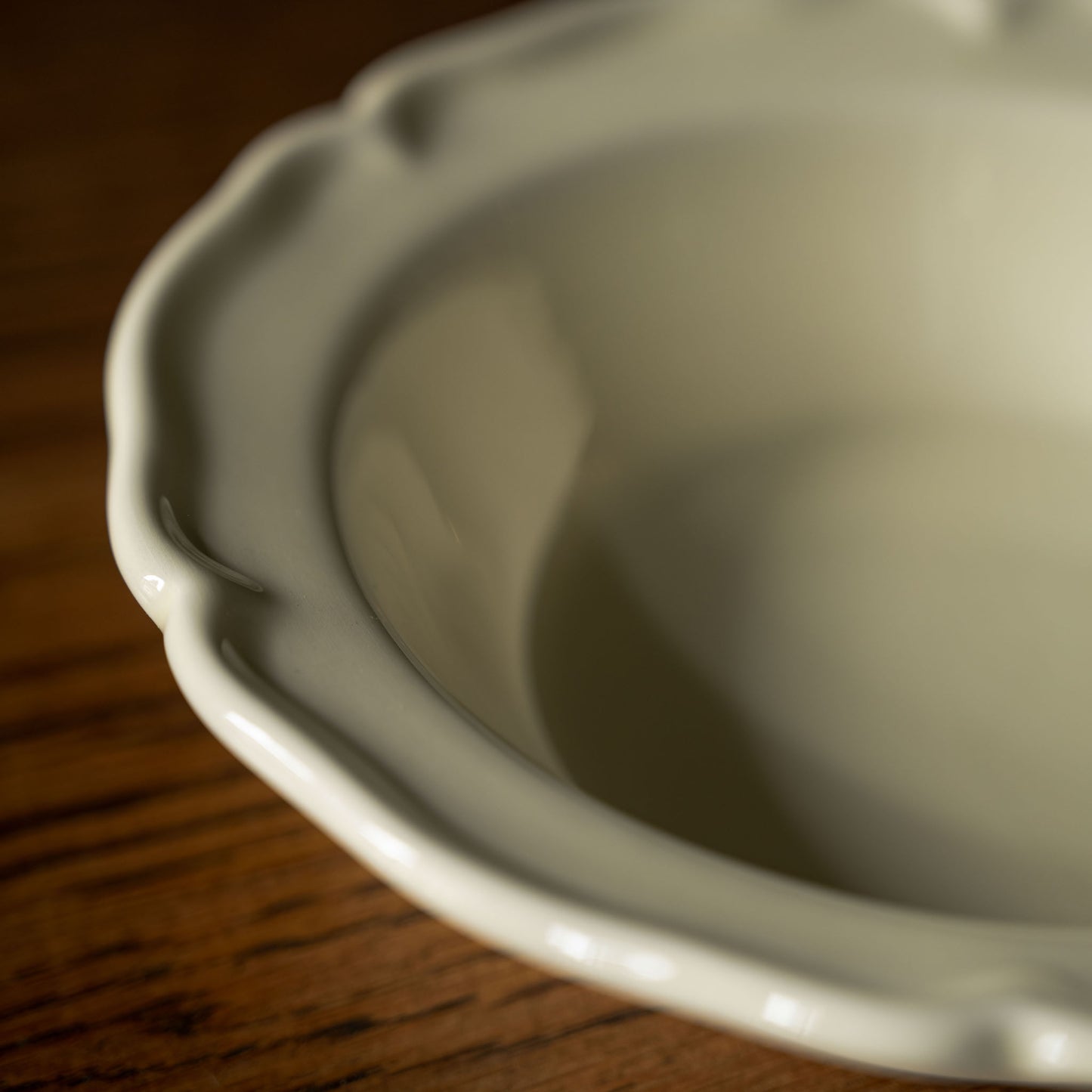 Close up of scalloped rim design on glossy cream pottery small bowl 