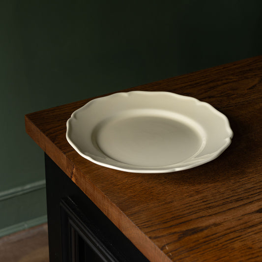 Glossy cream pottery dinner plate with scalloped rim design