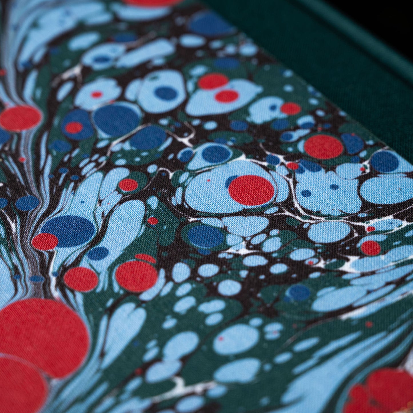 Close-up of Wainwright Bookbinding notebook cover with a colourful marbled pattern featuring blue, red, and dark green colours.