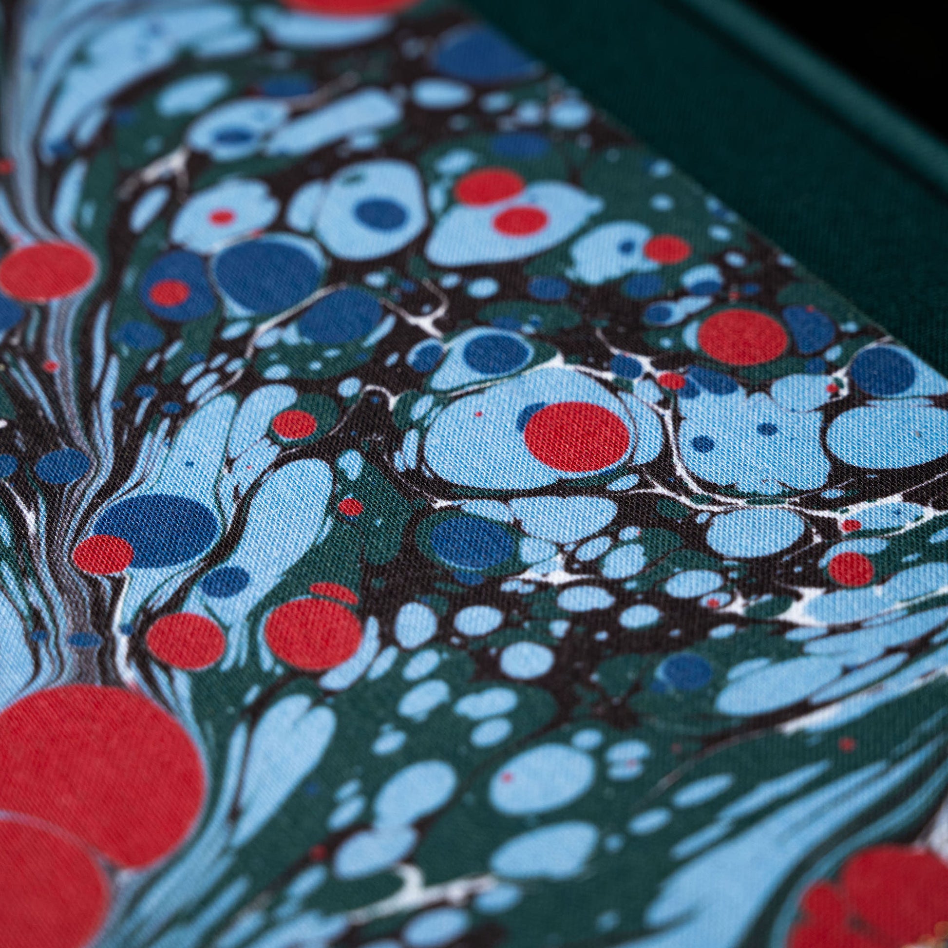 Close-up of Wainwright Bookbinding notebook cover with a colourful marbled pattern featuring blue, red, and dark green colours.